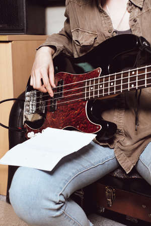 crop view of a young woman playing elecrtic guitar. bass guitarist reading chords notes and play in studio.の写真素材