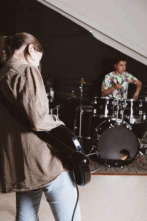 rock band rehearsal in a studio. female bass guitarist and teen male drummer performing a song. vertical size.の写真素材