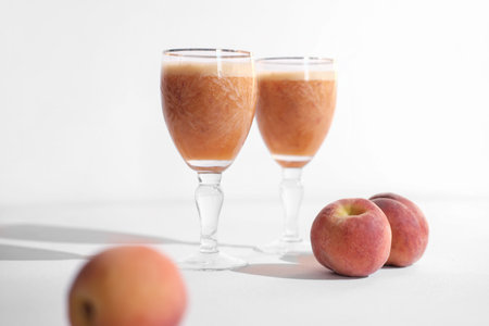 peach smoothie in glasses and three peaches on white background. healthy drinks for vitamin...