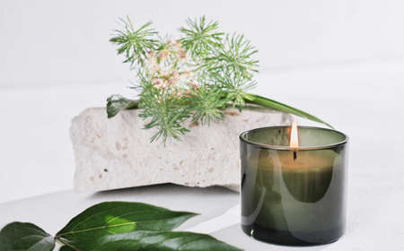 scented candle with herbal fragrance, natural stone and green leaves and grass on white table. cozy house conceptの写真素材