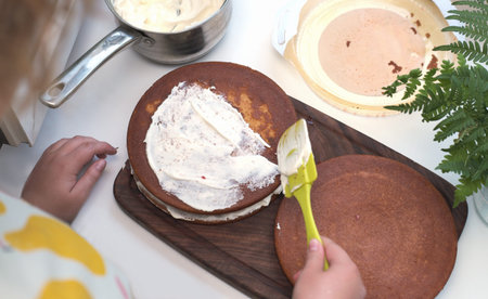 teenager girl's hands making frosting of a sponge cake. homemade pastry, hobby for teens on...