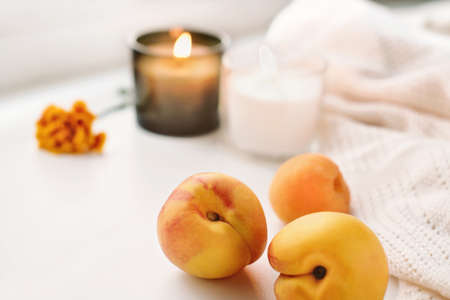 fresh ripe peaches, candles and flower next to warm knitted plaid. autumn cozy home concept.fall mood.の写真素材