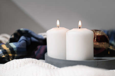 two white burning candles on a concrete tray and warm winter scarf. cozy holiday and cold season atmosphere. merry christmas and happy new year concept.の写真素材