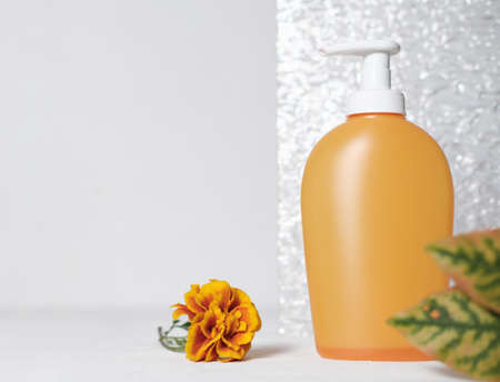 fall cosmetic product in orange container with pump.shower gel or liquid soap next to glass bathroom door and orange flower. fall product sale concept.の写真素材