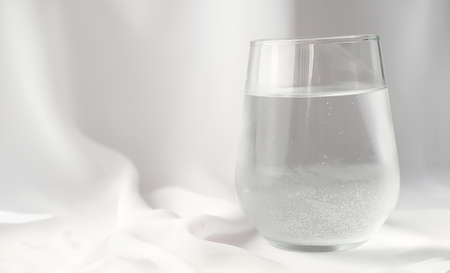a glass of sparkling mineral water white silk background. water drinking, morning rituals, trendy styled compositionの写真素材