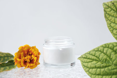 white protective face cream in a glass jar. autumn flowers and leaves. cold protection concept. skin...