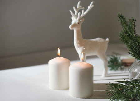 christmas home decor, burning white candles and reindeer next to christmas tree branches. happy holiday at homeの写真素材