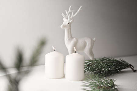 christmas home decor, burning white candles and reindeer next to christmas tree branches. happy holiday at home, interior decoration with traditional x-mas eve symbolの写真素材
