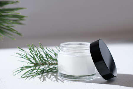 cold protection cream for dry skin. winter soothing and nourishing treatment for face care. white glass jar next to pine branchesの写真素材