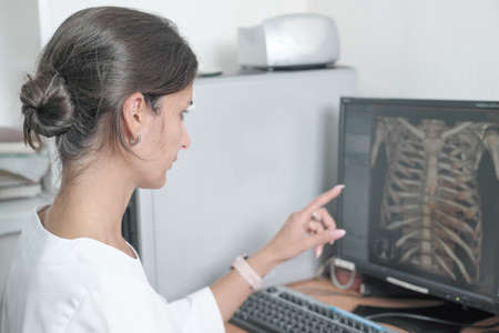 middle east woman doctor looking at monitor with chest bones computer tomography image and pointing at details. female young radiologist discussing ct test resultsの写真素材