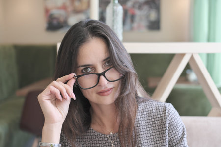 asian or middle east woman wearing eyeglasses looking at camera and touching her eyeglasses. getting...