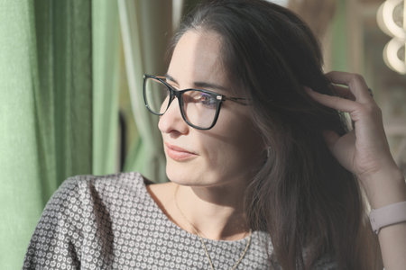 asian or middle east woman wearing eyeglasses looking aside and touching her hair. getting rest or...