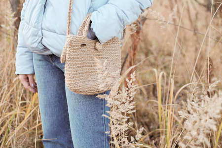 Handmade natural jute knit shopping bag, scandinavian style, beige tones, sustainable fashion accessories. Zero waste lifestyle. Woman standing in a field with DIY jute bagの写真素材