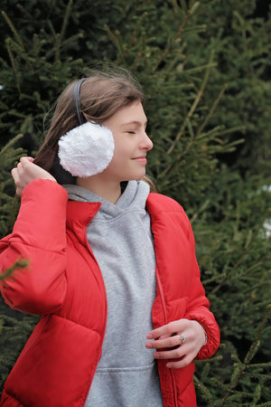 teenager girl wearing red jacket and earcuffs touching her hair while standing next to christmas...