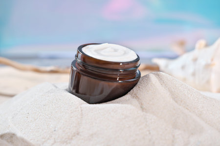 face cream in amber glass jar on a sandy beach. summer face care and UV protection for sensitive...