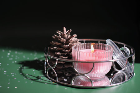 glowing scented candle on a mirror tray next to a pine cone on green background. christmas and new year celebration, home decot for holidayの写真素材