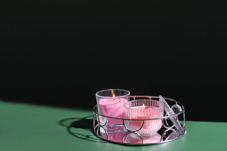 two pink scented candles on mirror metallic tray. glowing aromatic candels on green backgound. cozy evening home atmosphere. copy space.の写真素材