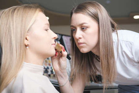 woman make up artist applying face powder on model's face in a beauty salon. skin color correction, visagiste working on female make-upの写真素材