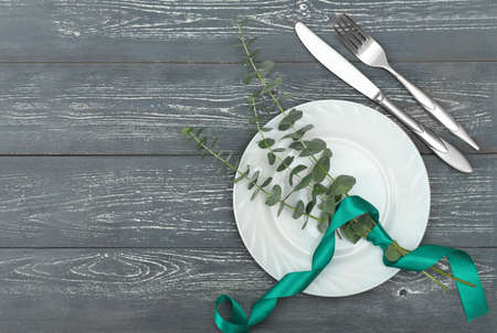 Spring elegant table setting, spring restaurant menu concept. top view of white dishes and silverware next to eucaliptus branches on a grey rustic table.の写真素材