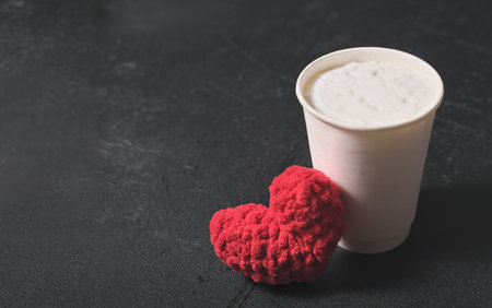 carton cup of coffee with whipped cream and knitted red heart on black background. copyspace. coffee to go. valentines day and love conceptの写真素材