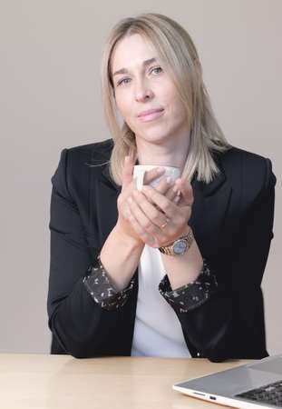 woman attorney or financial consultant or lawer wearing formal suit holding a cup of coffee looking at camera. confident sucsessful woman sitting by the desk with laptop. verticalの写真素材
