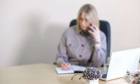 defocused background woman in office speaking by phone and making notes. copy space, blurred image.の写真素材