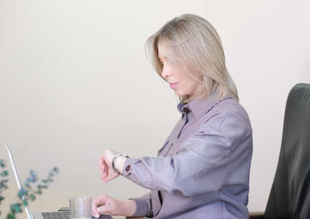 woman working in office and looking at watch, overworking, overloading. deadline, timing and checking appointmentの写真素材