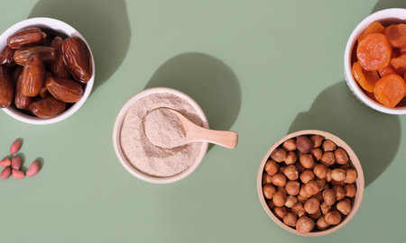 dates, dried apricots and nuts in mini bowls on green background. nut flour. healthy snack for...
