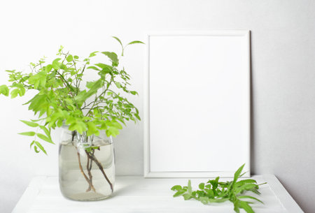 summer mockup with white frame copy space and green branches in a vase on a table. blank frame for inscription, selective focus.の写真素材