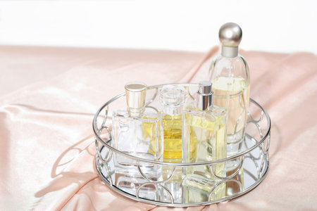 various bottles of perfume on a trendy mirror tray. pink silk satin fabric background. perfume set. fragrances for women.の写真素材