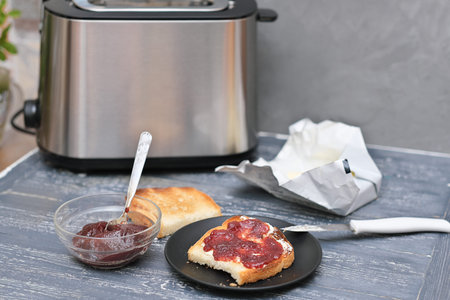toasts with butter and berry jam on a wooden table next to toaster. breakfast time