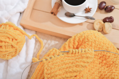 knitting scarf with needles using yellow yarn. cinnamon coffee in a white cup and dry fruits. autumn...