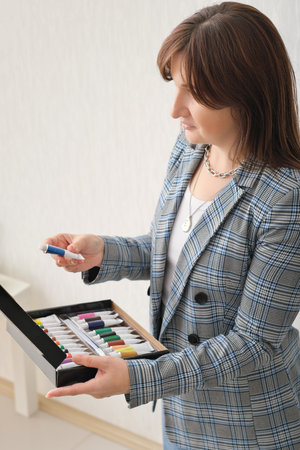 woman teacher of art holding a box with acrylic paints and taking one of the tubes. art teaching in school, creative hobby and learning to draw.の写真素材