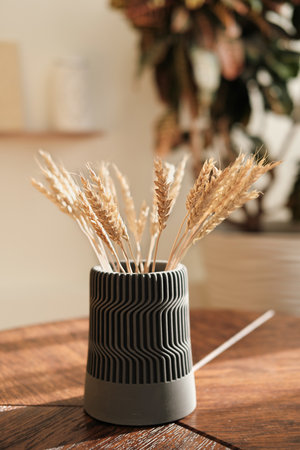 Stalks of dry wheat in concrete vase on wooden table. Wheat spikelets. backlit details of home decor in scandinavian minimal style.の写真素材