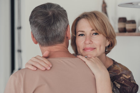 middle age woman embracing her husband and looking at camera. beautiful woman at her 50s, happy and relaxed with a man turned back.の写真素材