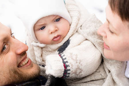 Cropped view of the pretty caucasian couple with dark hair posing with their beautiful newborn baby at the street and enjoying time with him. Cute child between of his parentsの写真素材