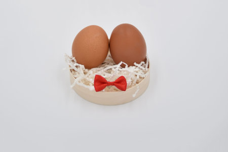Two brown eggs together on the white crumped paper cuts with the red bows