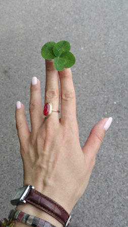 female hand with four leaves clover and a golden ruby ring on the middle finger