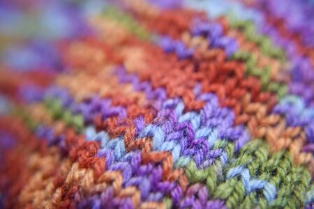 Selective focus at the bright colorful knitted pattern close-up look. Natural wool of red, orange, green, blue, purple colors.の写真素材