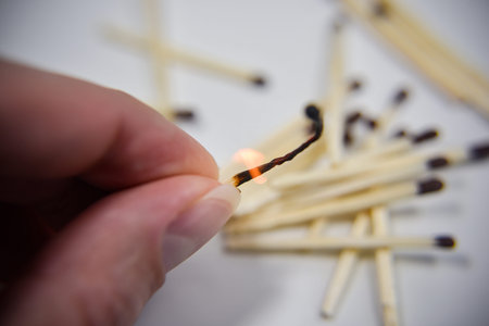 Burning wooden match in the hand with matches on the white backgtound. Selective focus. Chain...