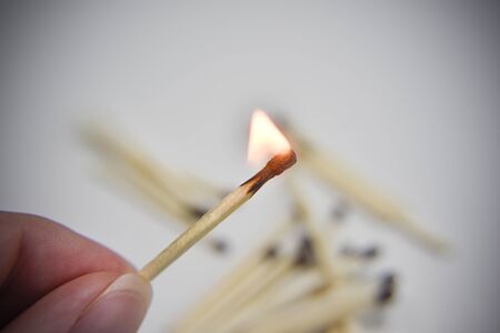 Burning wooden match in the hand with matches on the white backgtound. Selective focus. Chain reaction concept.の写真素材