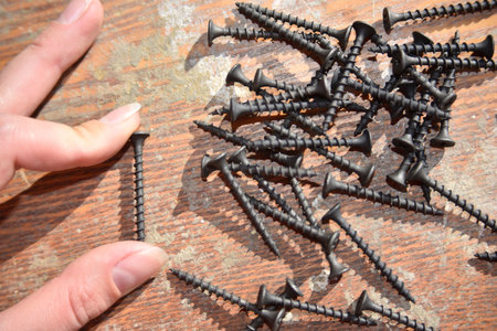 selective focus at the female hand with long nails, holding black screws, concept of work, close-upの写真素材