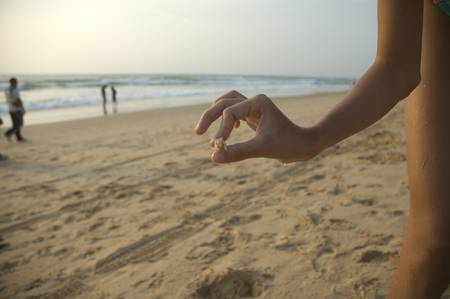 The child gently holds the shrimp in his fingers against the background of a huge ocean at sunsetの写真素材