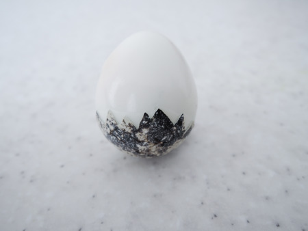 One semi-peeled egg a little in a shell on a marble background.の写真素材