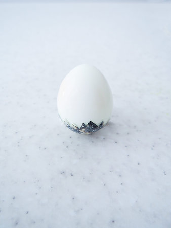One semi-peeled egg partially in a shell on a marble background.の写真素材