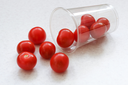 Several bright red ripe cherry tomatoes rolled out of a plastic transparent glass.の写真素材
