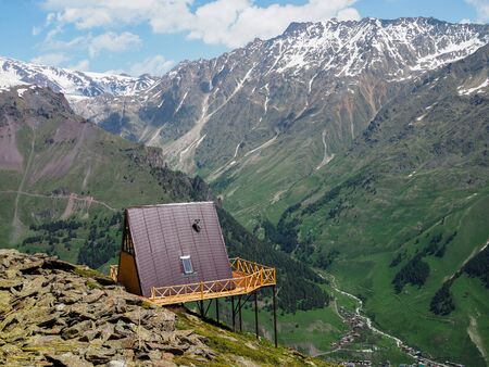 single wooden house with a red roof on a hill high in the mountains with a beautiful view of the green valley on a Sunny day.の写真素材