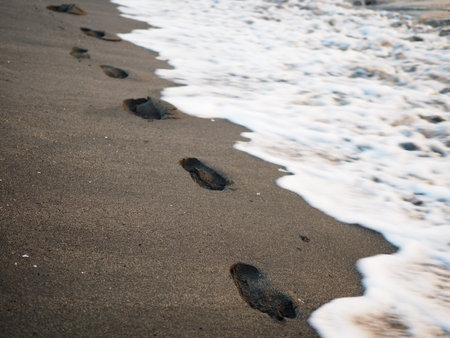 foot prints on a black sand beach with tilt-shift blur. Surf in background. Concept for loneliness,...