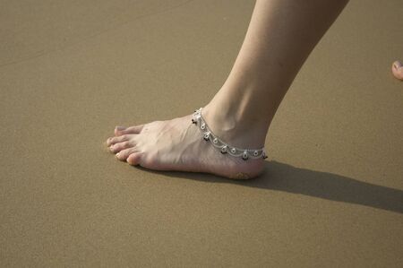 Closeup of a woman's legs with an anklet jewelry on the beach.の写真素材