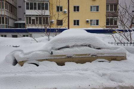 City street after blizzard. Stuck cars under the snow and ice. Buried vehicle in snowdrift on the road. Parking lots in winter after heavy snowfall. Uncleaned roads. Record-breaking amounts of snowの写真素材
